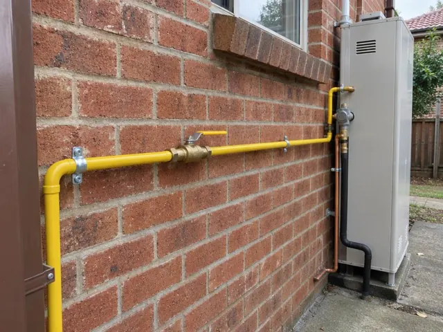 Yellow gas piping on a brick exterior wall beside a home appliance in Ryde